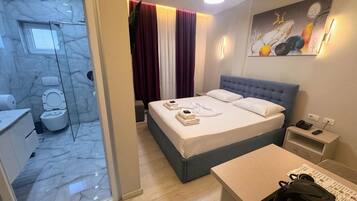 A hotel room with a bed, bedside table, and a small desk with a kettle.
