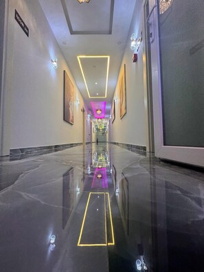 Un pasillo de hotel con piso pulido, obras de arte enmarcadas en las paredes y un cartel que indica la dirección a la habitación.