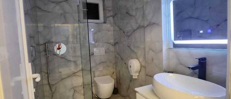 A bathroom with a marble wall, a glass shower enclosure, a toilet, and a vanity with a sink.