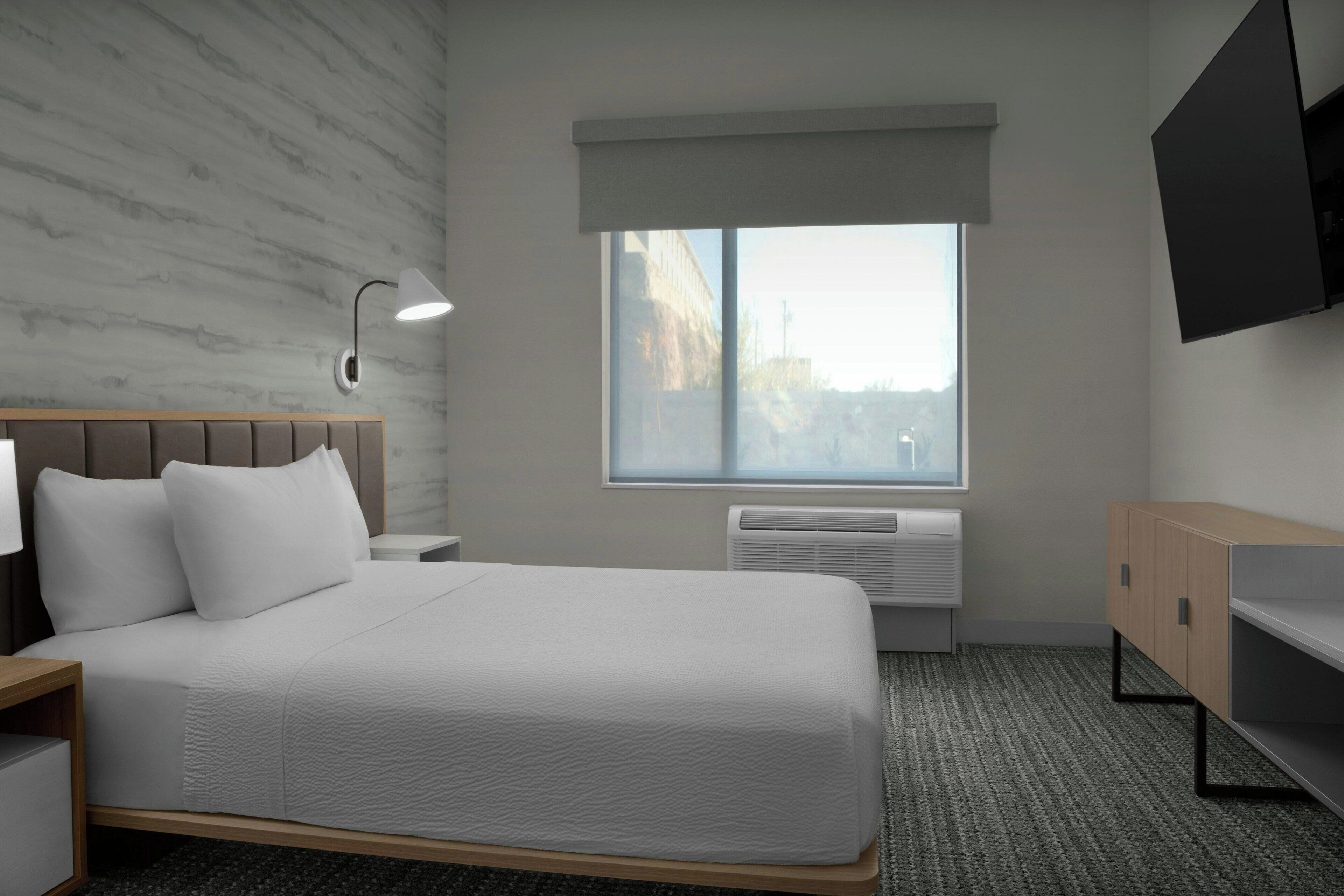 Une chambre d’hôtel équipée d’un lit, d’une table de chevet, d’un bureau, d’une télévision, d’une fenêtre avec vue et d’un appareil de climatisation.