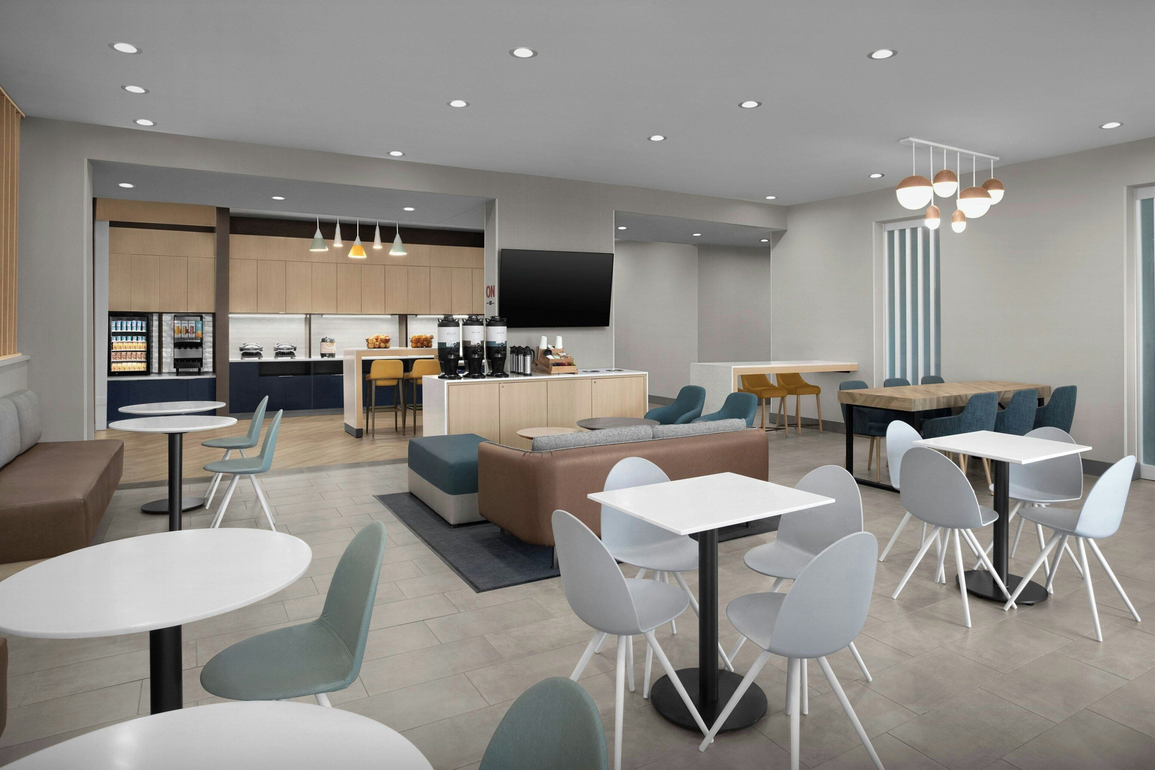 A modern hotel lobby with seating areas, a kitchen, and a flat-screen TV.