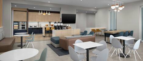 A modern hotel lobby with seating areas, a kitchen, and a flat-screen TV.