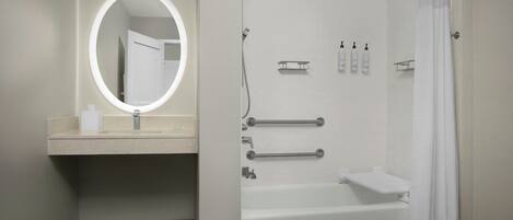A modern bathroom with a round mirror, a bathtub, and a shower area.