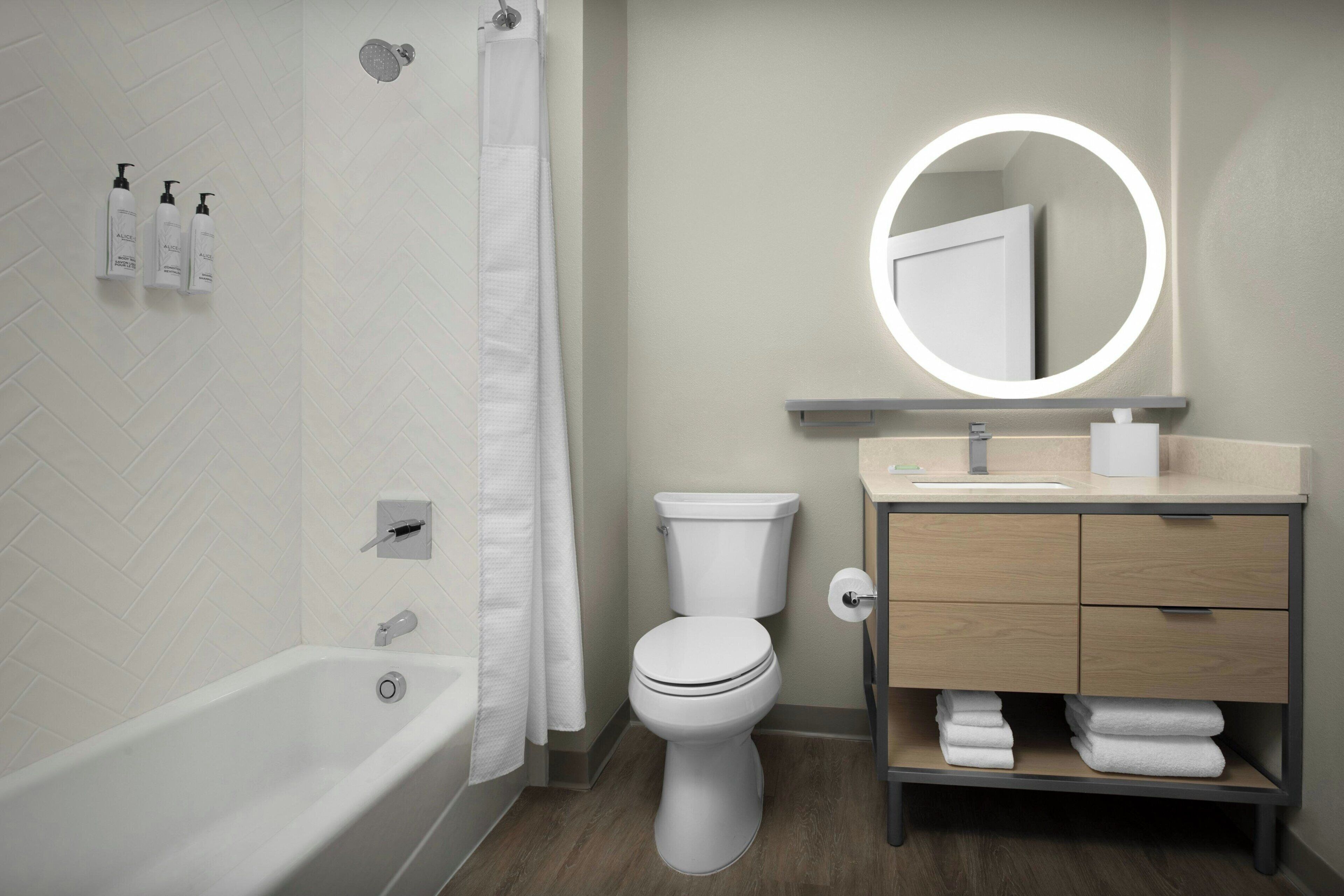 A modern bathroom with a bathtub, toilet, vanity with a mirror, and toiletries on the wall.