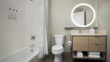 A modern bathroom with a bathtub, toilet, vanity with a mirror, and toiletries on the wall.