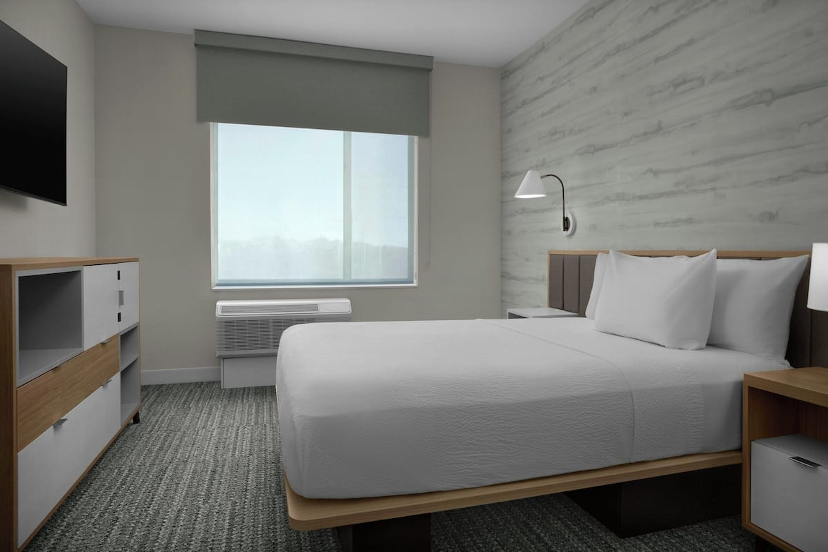 A hotel room with a bed, bedside tables, a TV, a window, and a wall-mounted lamp.