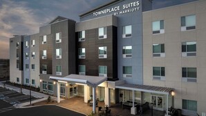 Ein mehrstöckiges Hotel im modernen Stil, mit überdachtem Eingangsbereich mit Sitzgelegenheiten und einem Parkplatz.
