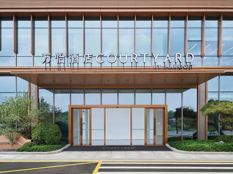 A modern hotel entrance with large glass windows and a sign reading "万怡酒店COURTYARD BY MARRIOTT".