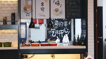 En restauranginteriör med en neonreklamskylt som visar texten ”SEND NOODLE”, en disk med olika rätter och tillbehör samt ett område med bord och stolar där gästerna kan sitta.