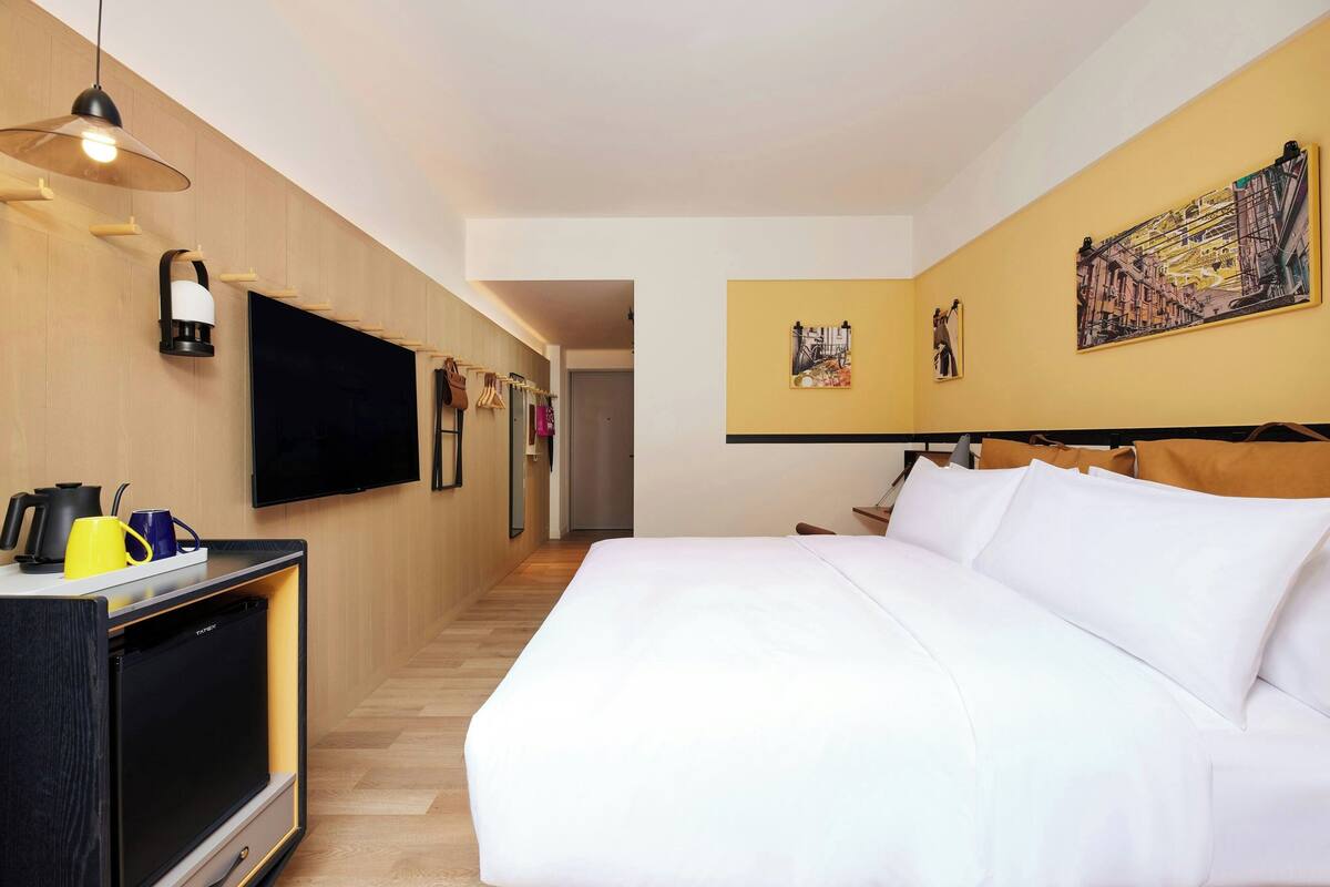 A hotel room with a bed, a flat-screen TV, a minibar, and artwork on the walls.