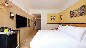 A hotel room with a bed, a flat-screen TV, a minibar, and artwork on the walls.