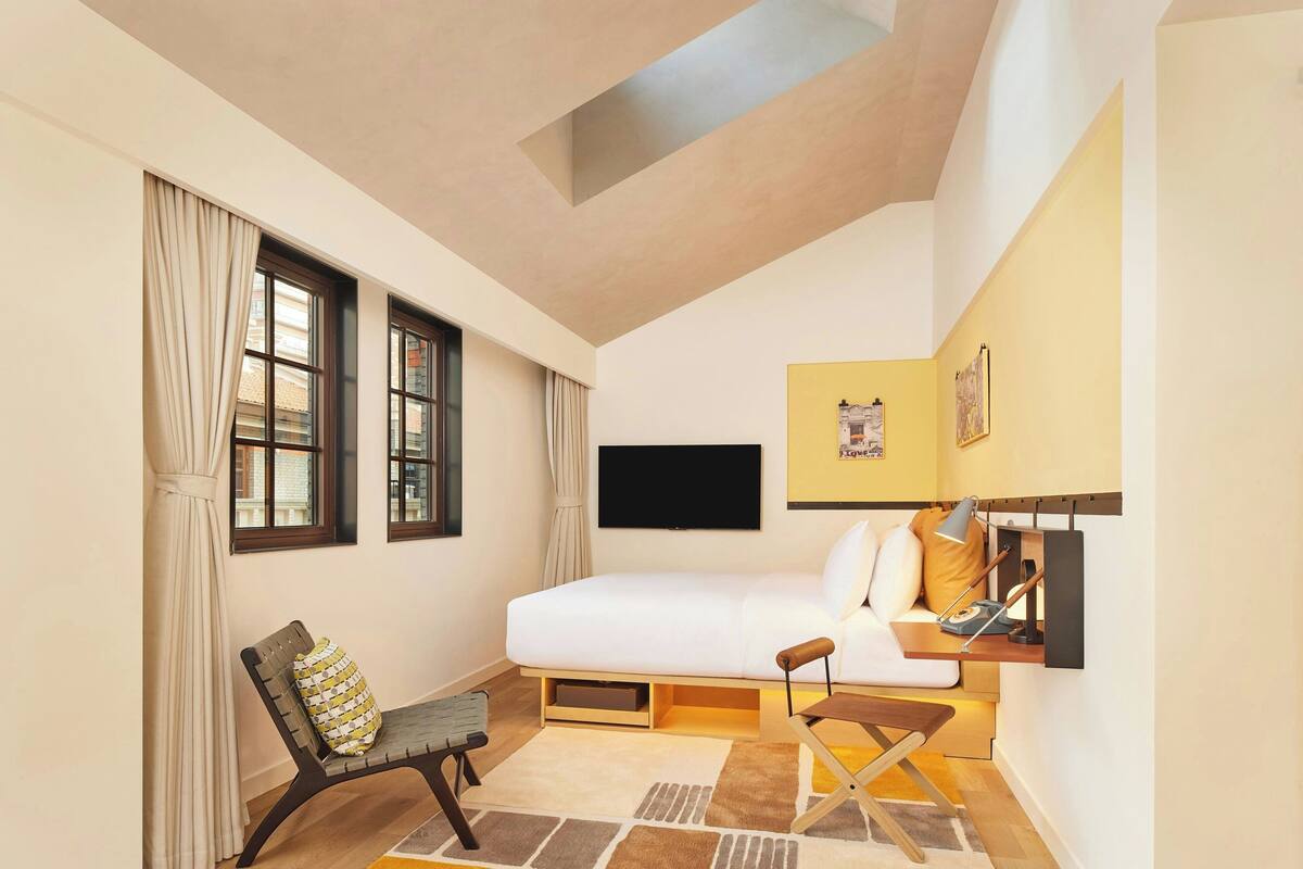 A bedroom with a bed, a desk, a chair, and a television on the wall.