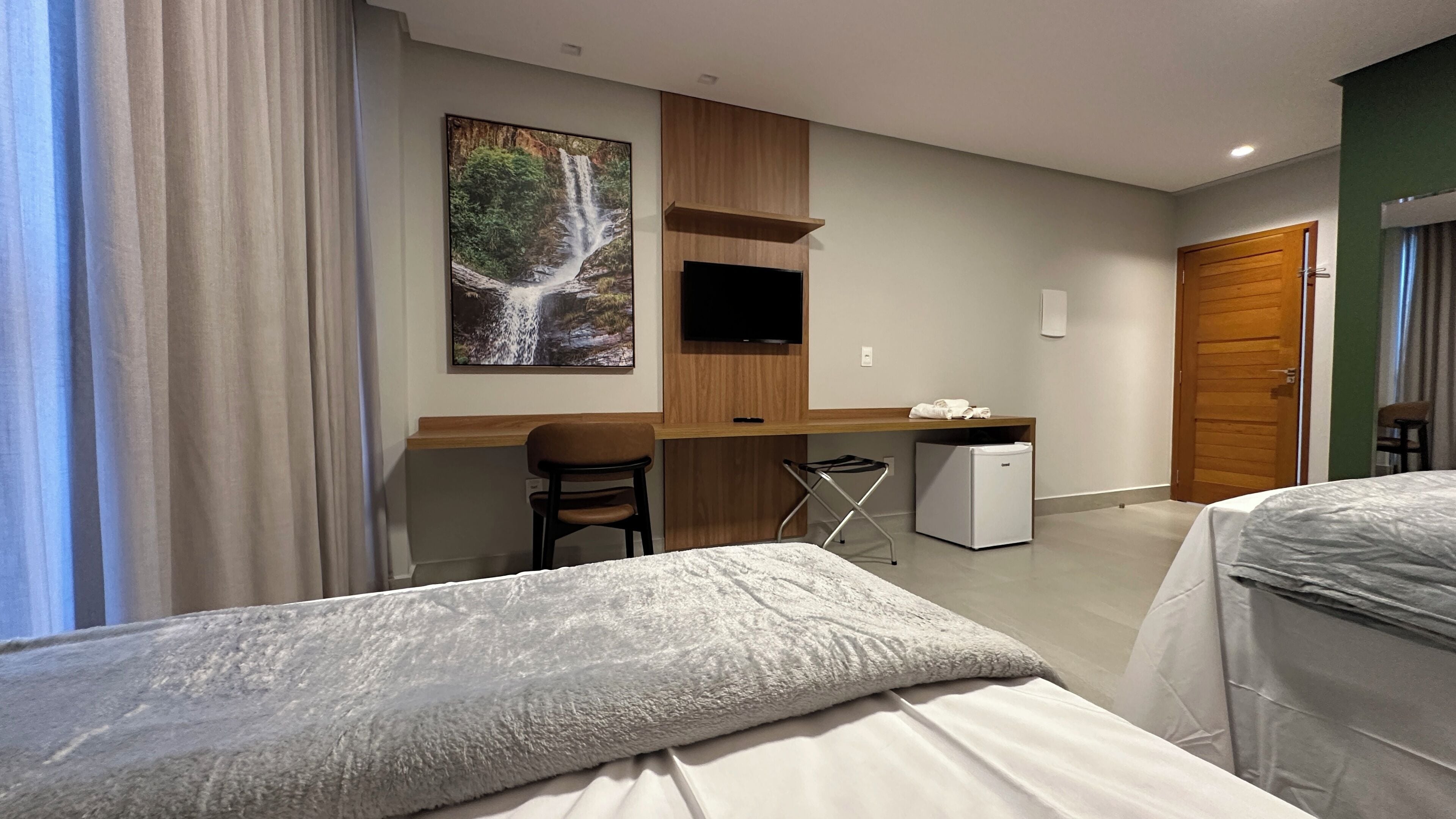 Habitación de hotel con cama, escritorio, silla, televisor y un refrigerador pequeño.