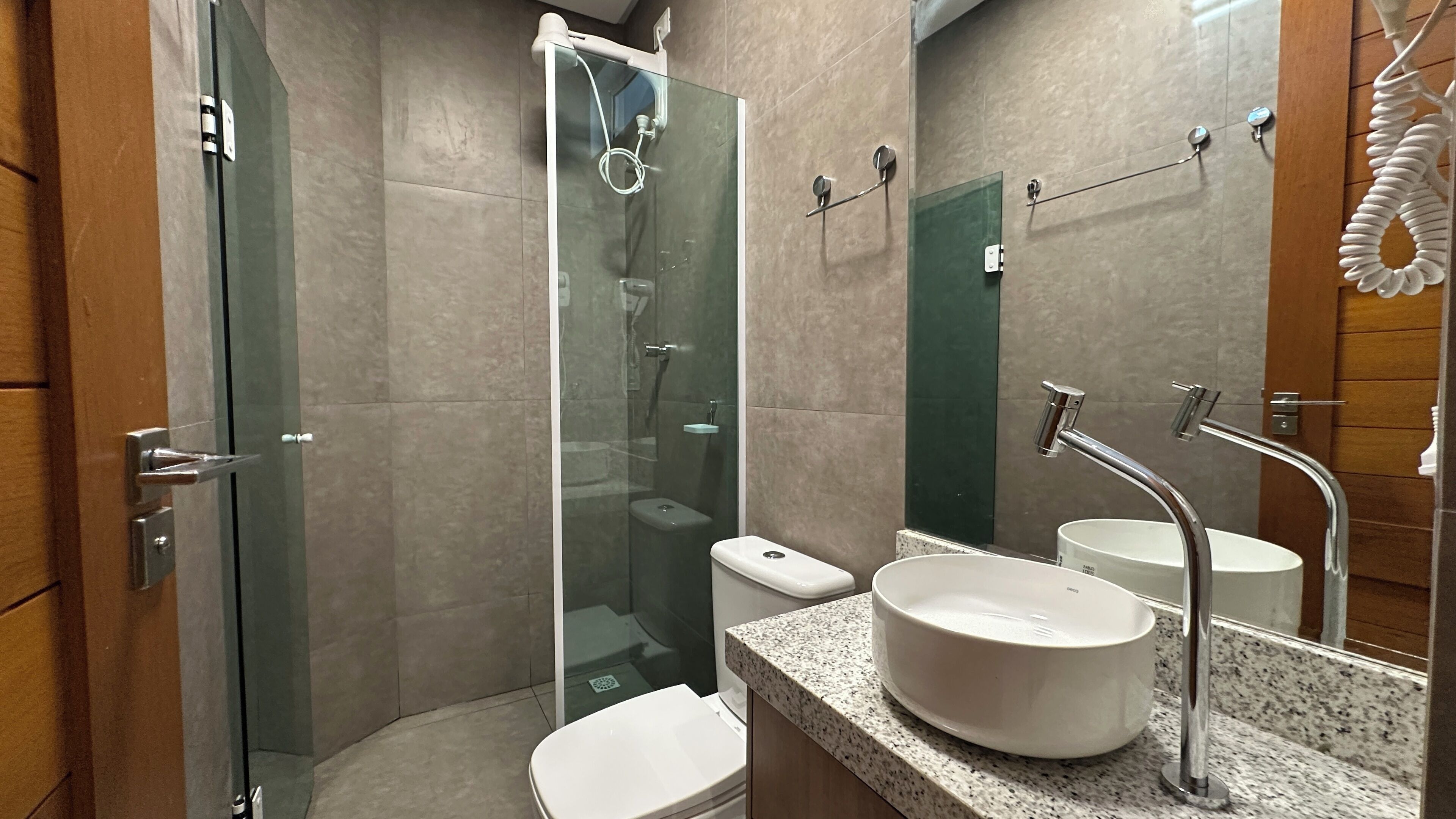 A modern bathroom with a glass-enclosed shower, a white toilet, a sink with a vessel basin, and a large mirror.