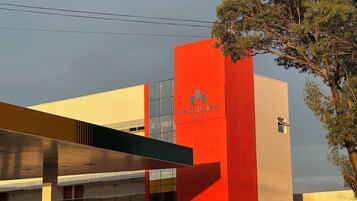 Un hotel moderno con una fachada roja destacada, entrada de vidrio y un árbol en primer plano.