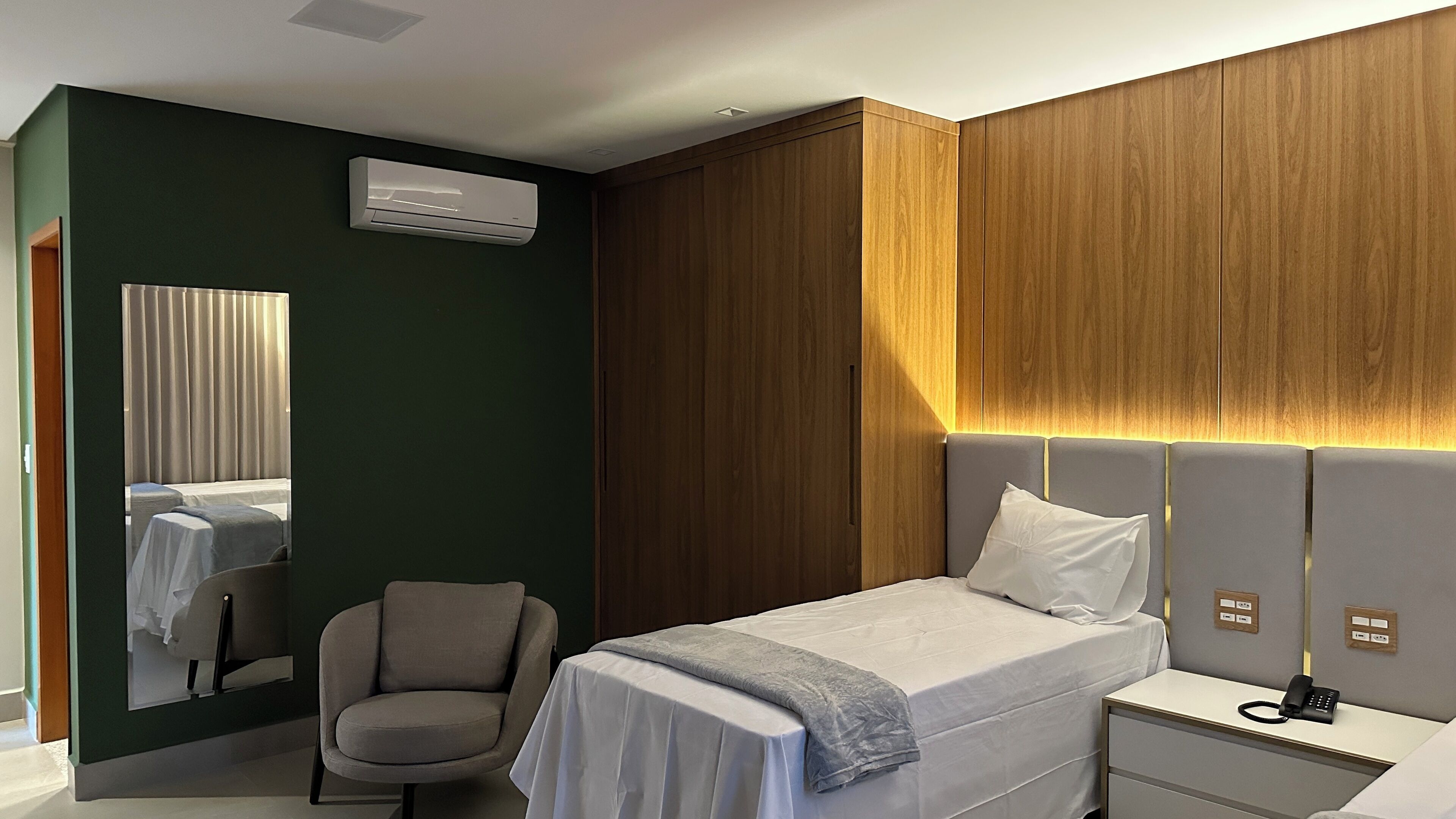 Ein modernes Hotelzimmer mit Bett, Nachttisch, Sessel und einem großen Spiegel.