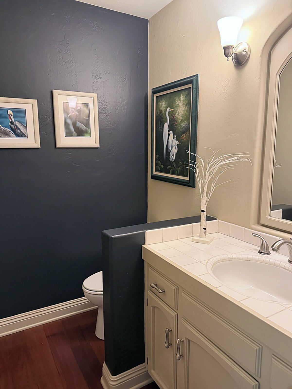 A bathroom with a dark blue wall, a white sink, and a toilet. There are three framed pictures on the wall.