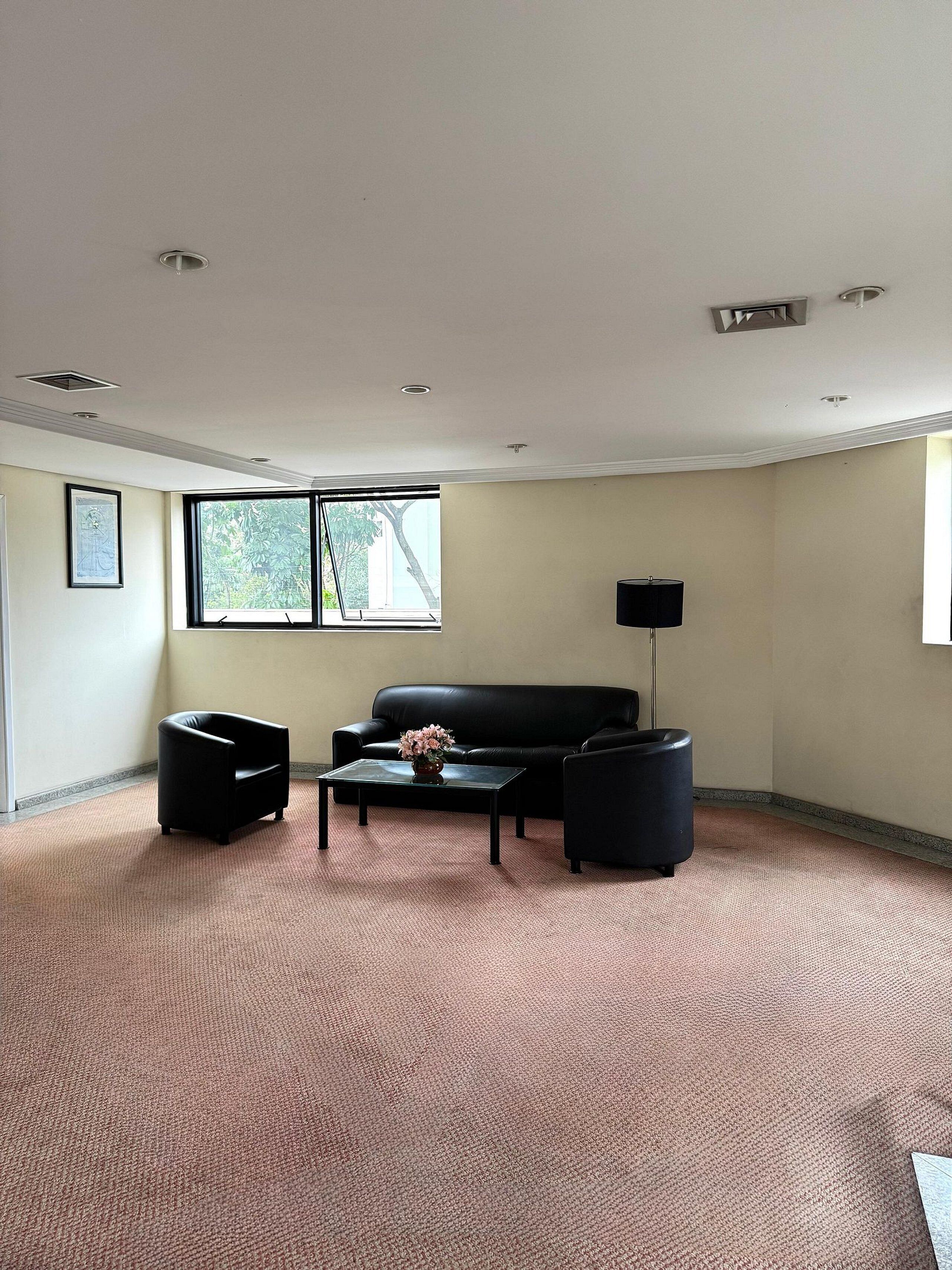 A spacious living room with a black leather sofa, a glass coffee table with a vase, and a black armchair.