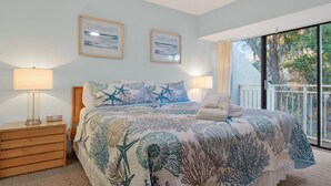 A bedroom with a bed, two bedside lamps, a nightstand, and a view of the outdoors through a balcony. - Sleeps 8!  2 Mins to Beach, 3 BD 3.5 BR- Sea Pines (Hilton Head Island)