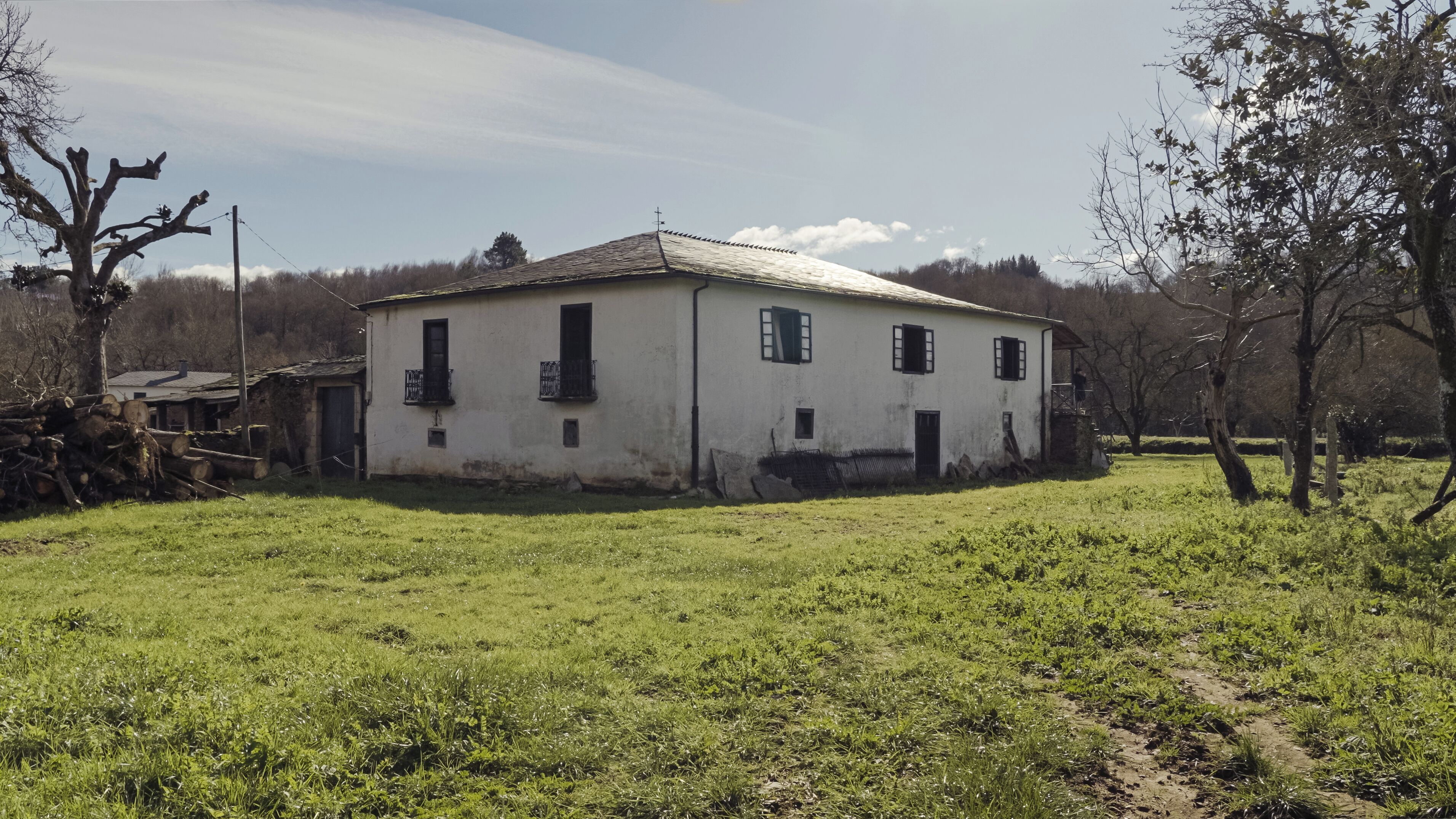 Um edifício branco com telhado inclinado, cercado por um campo gramado e árvores.