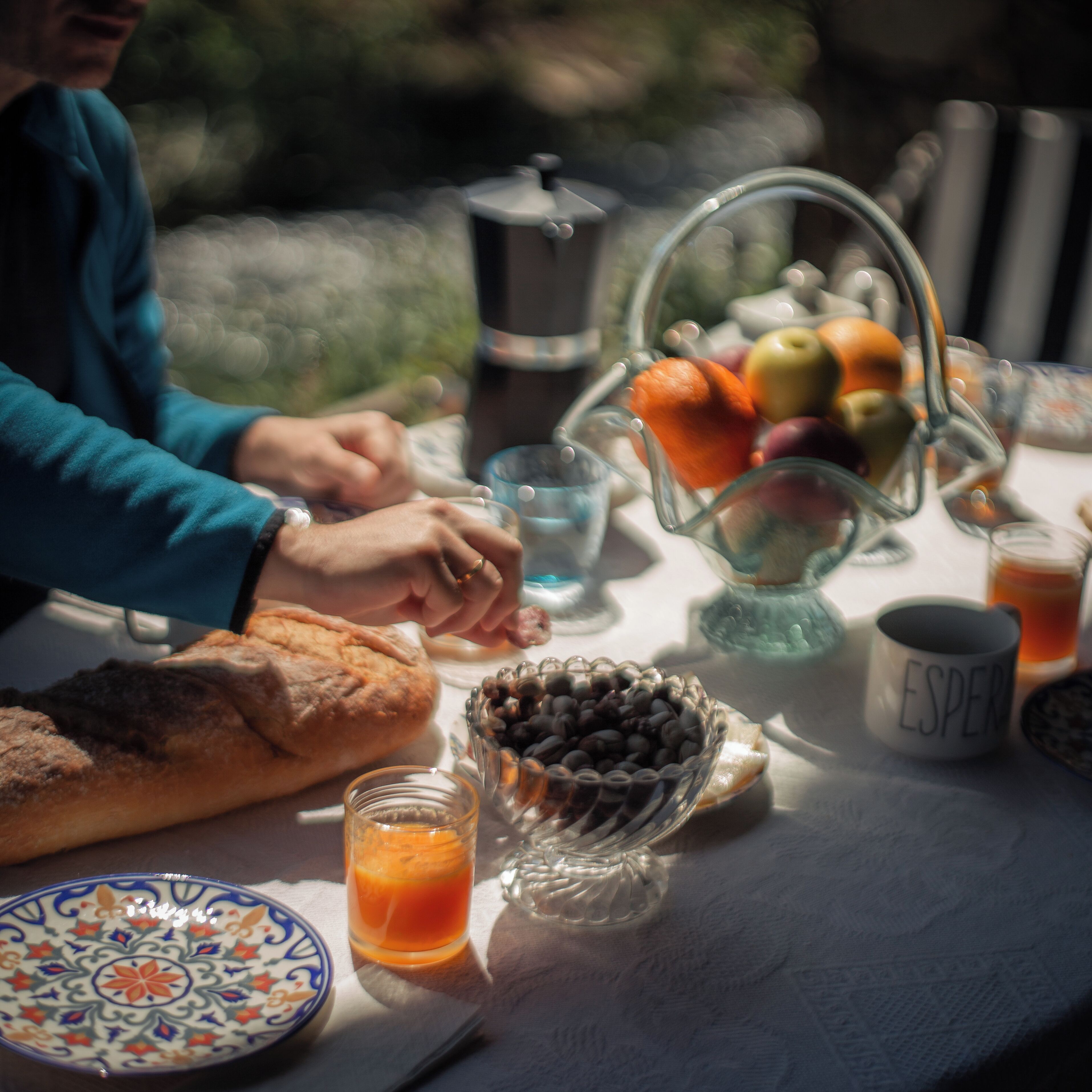 Una mesa de desayuno con pan, un bol de fruta, una cafetera y una taza con la palabra 'ESPRESSO'.