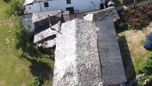 A white building with a stone roof, surrounded by greenery and a parked car. - House of Artists (Xullán)