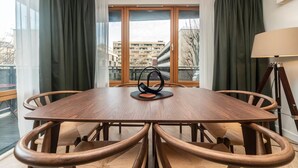 Un coin repas avec une table ronde et des chaises, de grandes fenêtres avec des rideaux et une vue sur les bâtiments environnants.