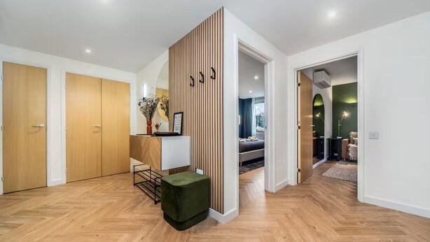 Un intérieur moderne avec des planchers en bois, un comptoir d’accueil, un pouf vert et une chambre à coucher comprenant un lit et un bureau.