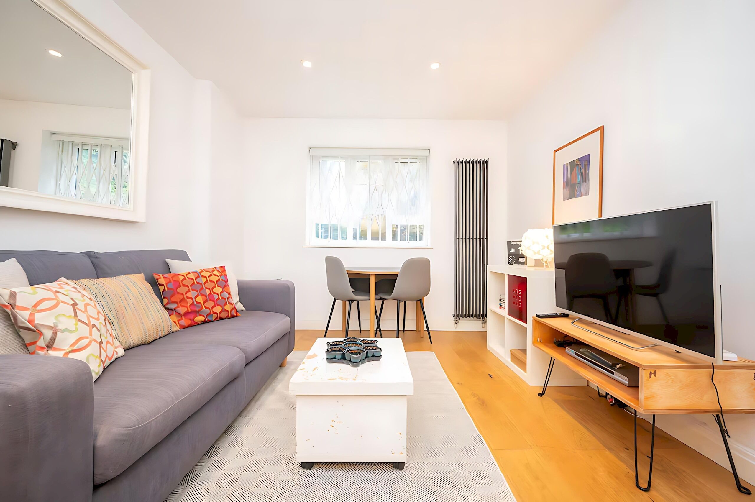 Una sala moderna con un sofá gris, una mesa de centro blanca, un mueble para televisión y un comedor con una mesa y sillas.