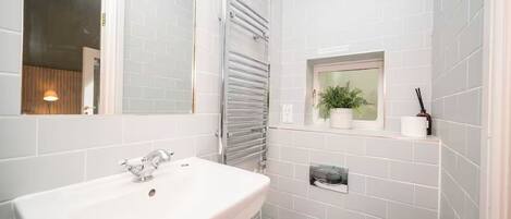 A modern bathroom with a white sink, a toilet, a window with a plant, and a towel rack.