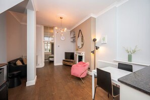 A modern living room with a wooden floor, a pink chair, a dining table, and a fireplace. - Cosy Retreat for Two off Upper St, Islington - Pass the Keys (London)
