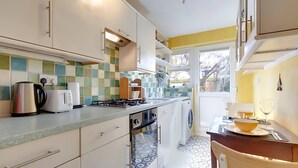 A modern kitchen with white cabinets, a gas stove, a kettle, and a washing machine. - Pass the Keys | Charming Ground Floor Flat with Free Parking (Cambridge)