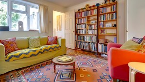 A cozy living room with a yellow sofa, a red armchair, and a bookshelf filled with books. - Pass the Keys | Charming Ground Floor Flat with Free Parking (Cambridge)