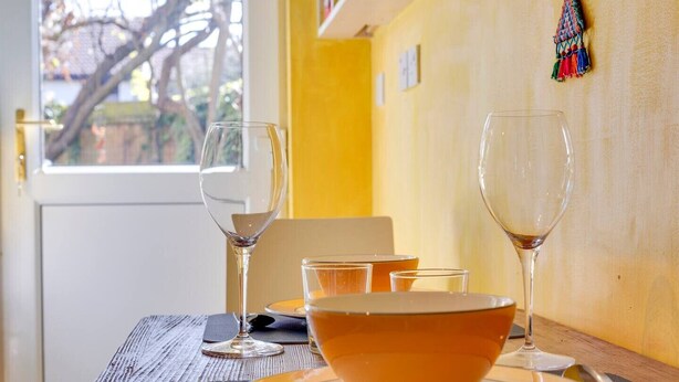 A dining table with a bowl and wine glasses, a window with a view of trees, and a yellow wall. - Pass the Keys | Charming Ground Floor Flat with Free Parking (Cambridge)