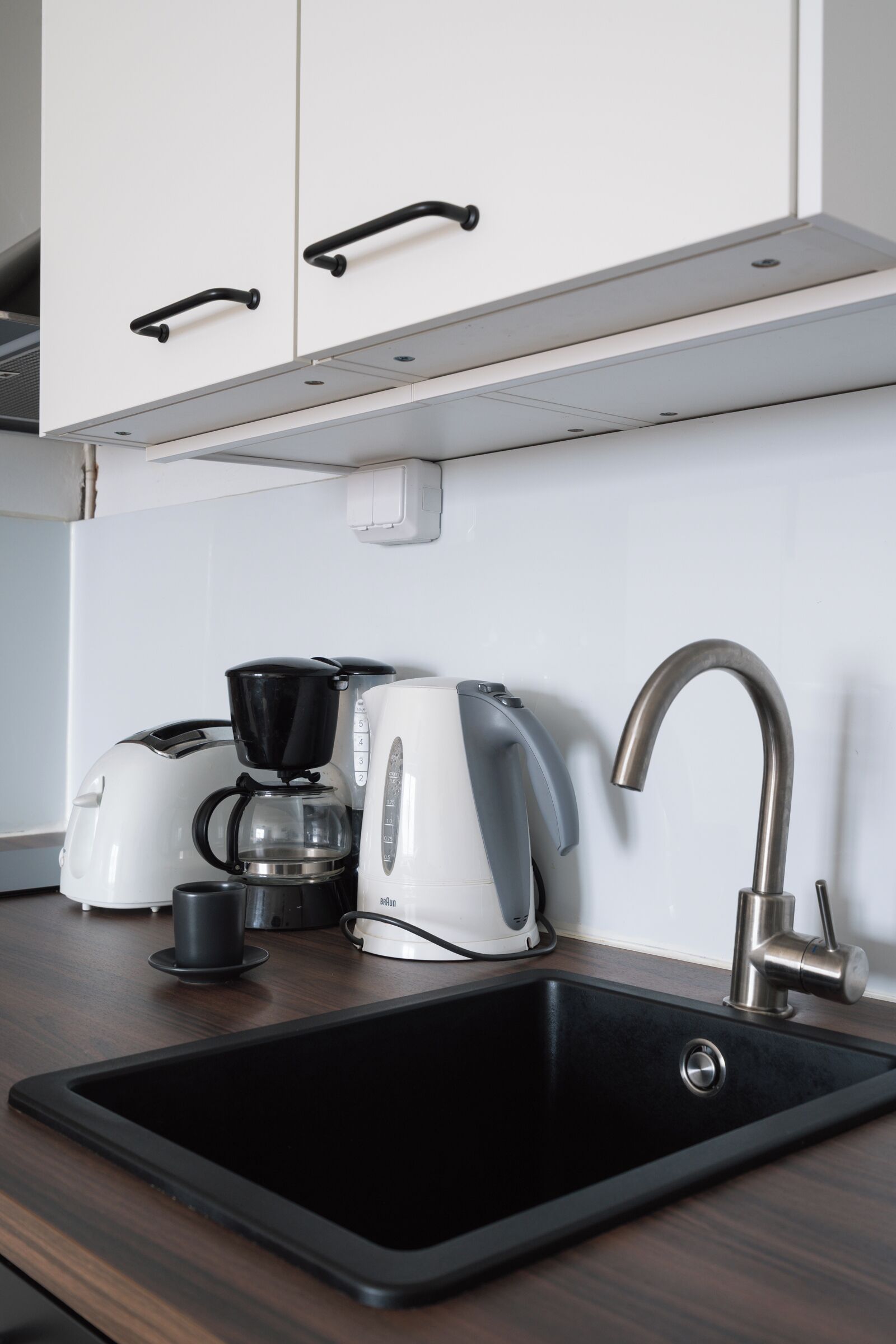 A kitchen with a black sink, a coffee maker, and a kettle on the counter.