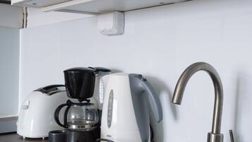 A kitchen with a black sink, a coffee maker, and a kettle on the counter.