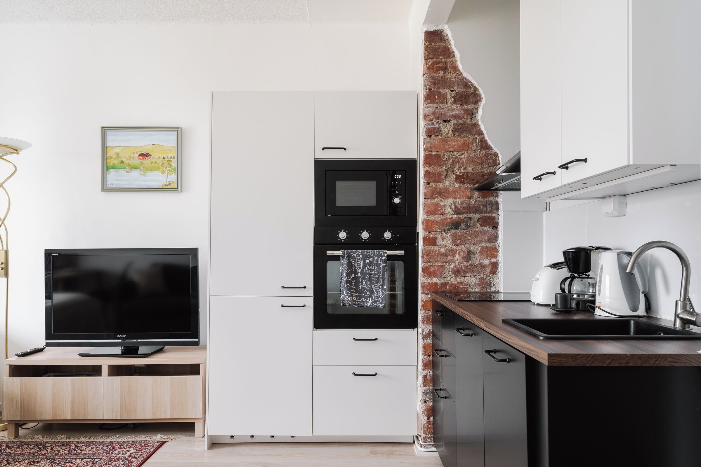 Een moderne keuken met een televisie, magnetron, oven en spoelbak.
