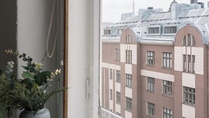 Une fenêtre donnant sur des immeubles, avec un pot de fleurs posé sur le rebord.