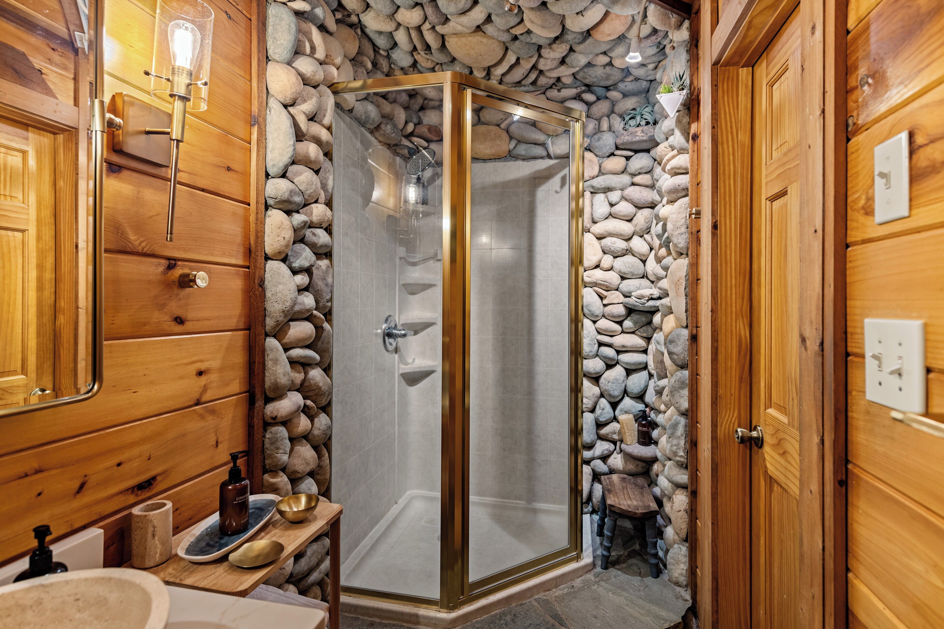 A wooden bathroom with a stone wall, a glass-enclosed shower, and a wooden door.