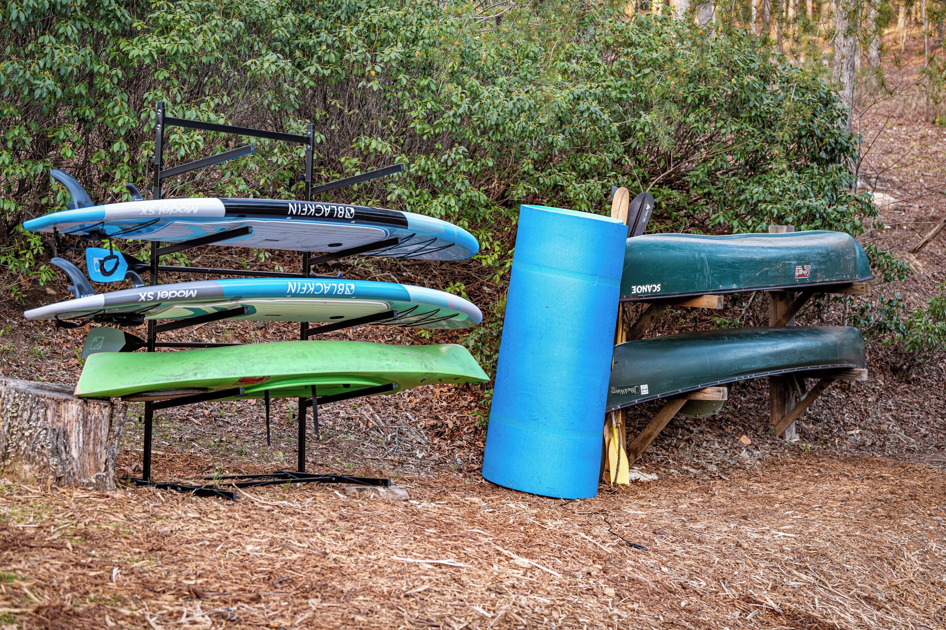 Kayaks and a canoe stored on racks and a stand in a wooded area.