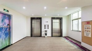 A hotel corridor with two elevators, carpeted flooring, a wall-mounted information board, and a large window on the right. - Lavande Hotels (Guangzhou Fangcun Huadiwan) (Guangzhou)