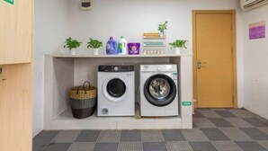 A laundry area with two washing machines, a shelf with plants and cleaning supplies, and a door with a sign. - Lavande Hotels (Guangzhou Fangcun Huadiwan) (Guangzhou)