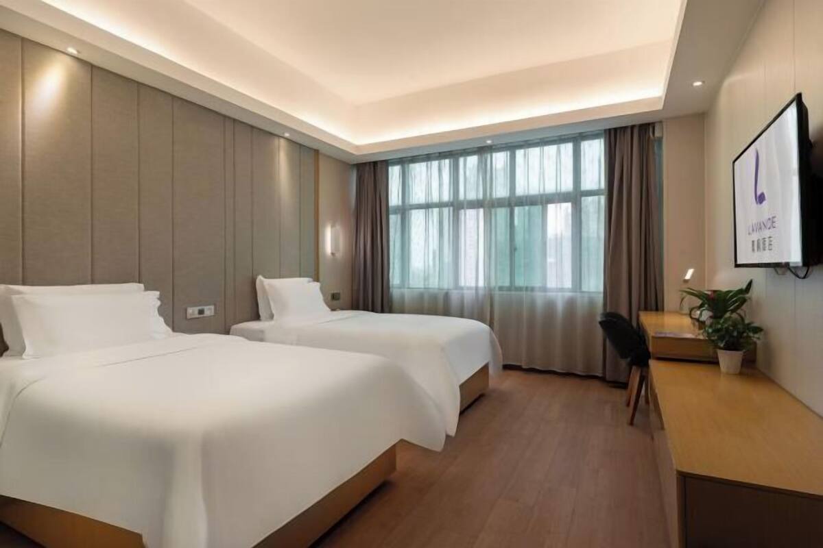 Ein Hotelzimmer mit zwei Betten, einem Schreibtisch, einem Stuhl, einem Fernseher und einem Fenster mit Vorhängen.