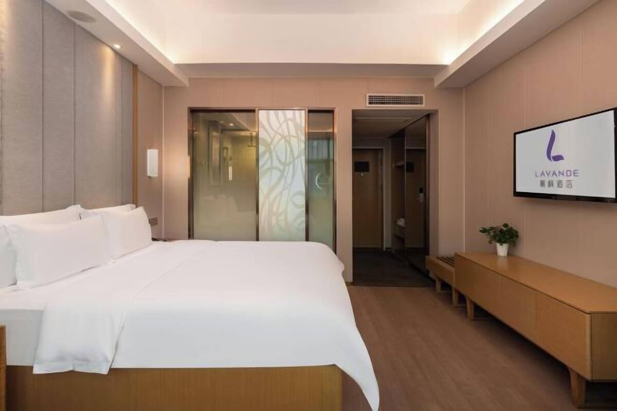Ein Hotelzimmer mit einem Bett, einem Nachttisch, einem Fernseher und einer Schiebetür zu einem Badezimmer.