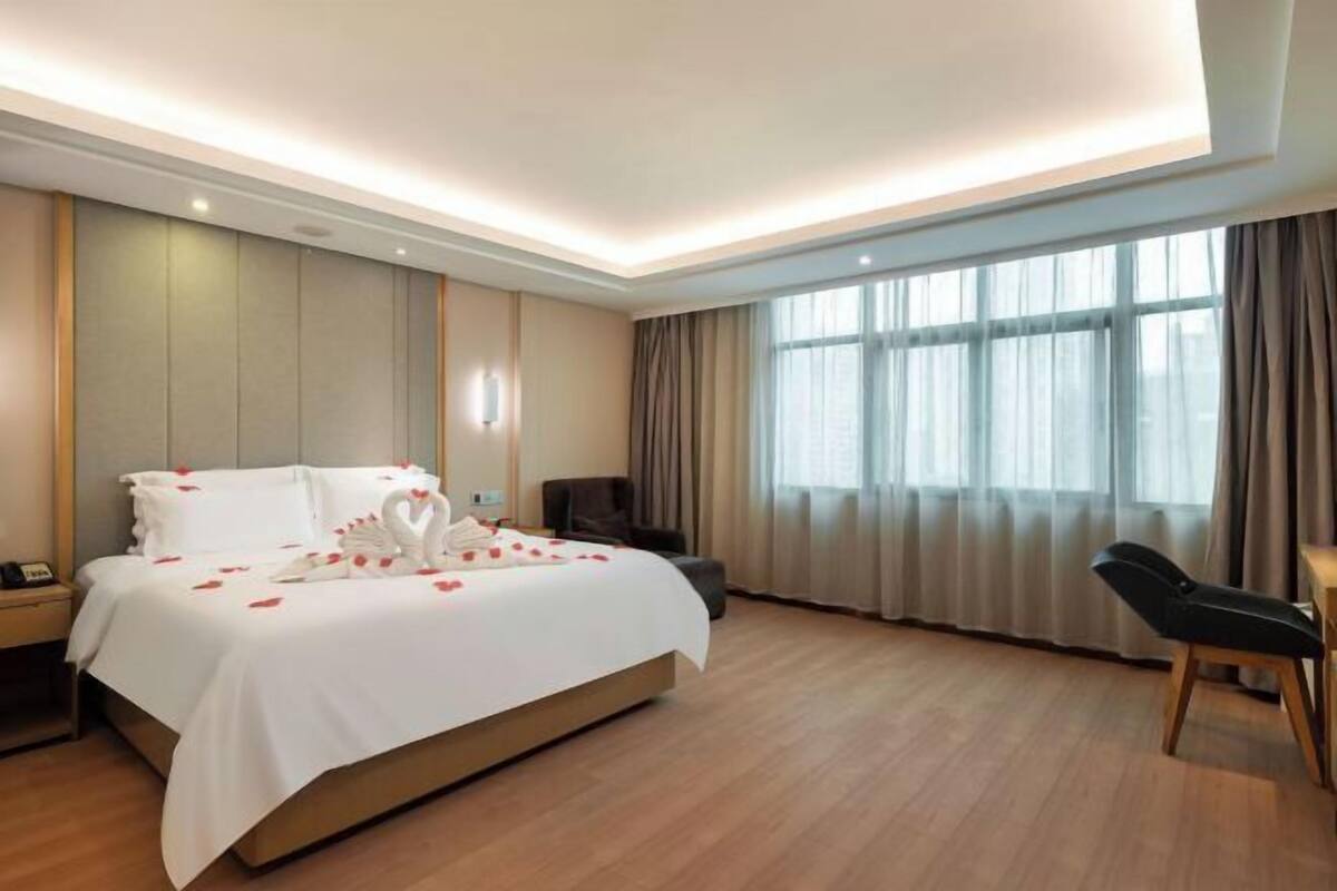 Ein Hotelzimmer mit Bett, Schreibtisch, Stuhl, Nachttisch und einem Fenster mit Vorhängen.