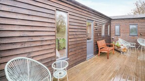 A wooden cabin with a deck, white wicker chairs, and a small table. - Willow Lodge 1 - UK48642 (Taunton)