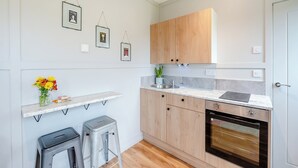 A modern kitchen with wooden cabinets, a marble countertop, a built-in oven, and a small bar stool. - Willow Lodge 1 - UK48642 (Taunton)