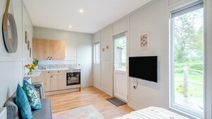 A modern bedroom with a large bed, a TV, and a view of a garden. - Willow Lodge 1 - UK48642 (Taunton)