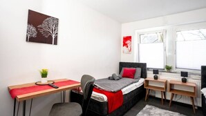 Une chambre à coucher de taille réduite, comprenant un lit, un bureau, une chaise et deux tables de chevet.