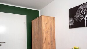 Une pièce avec une armoire en bois, une porte blanche, une moquette rouge et un tableau représentant un arbre accroché au mur.